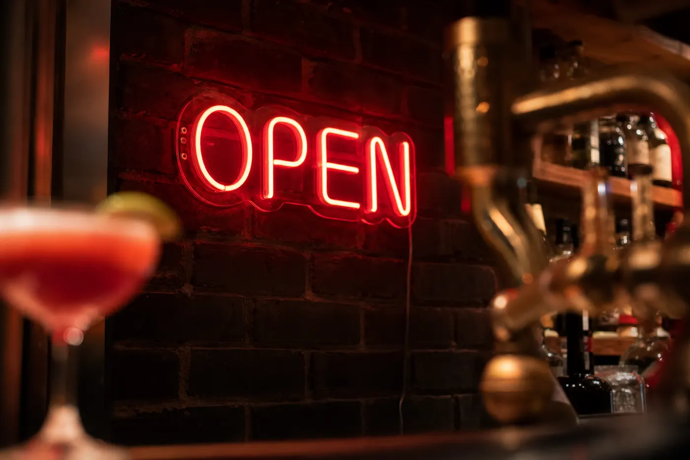 Red OPEN LED neon in a home bar with a blurred cocktail and brass tap