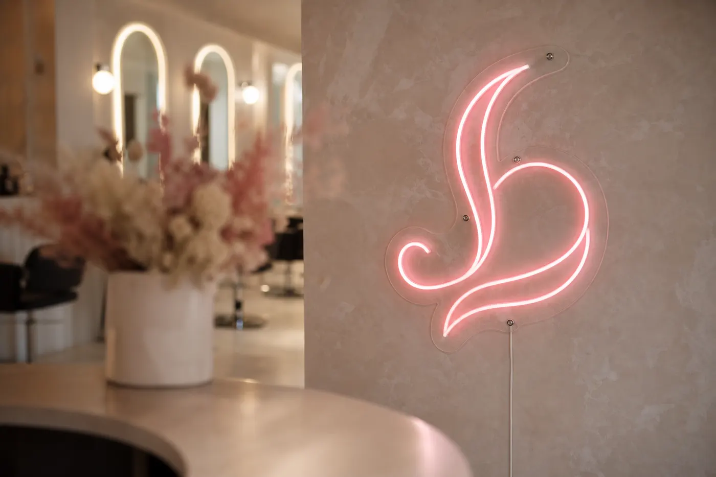 Soft pink abstract LED neon logo in a salon with blurred flowers