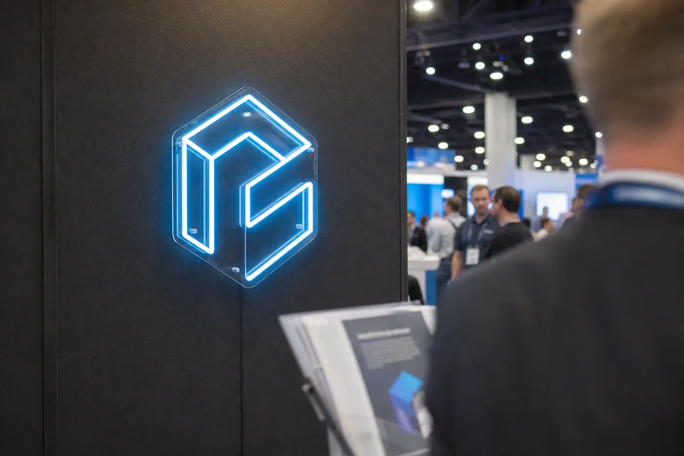 Ice blue geometric LED neon logo at a trade show booth with blurred visitors