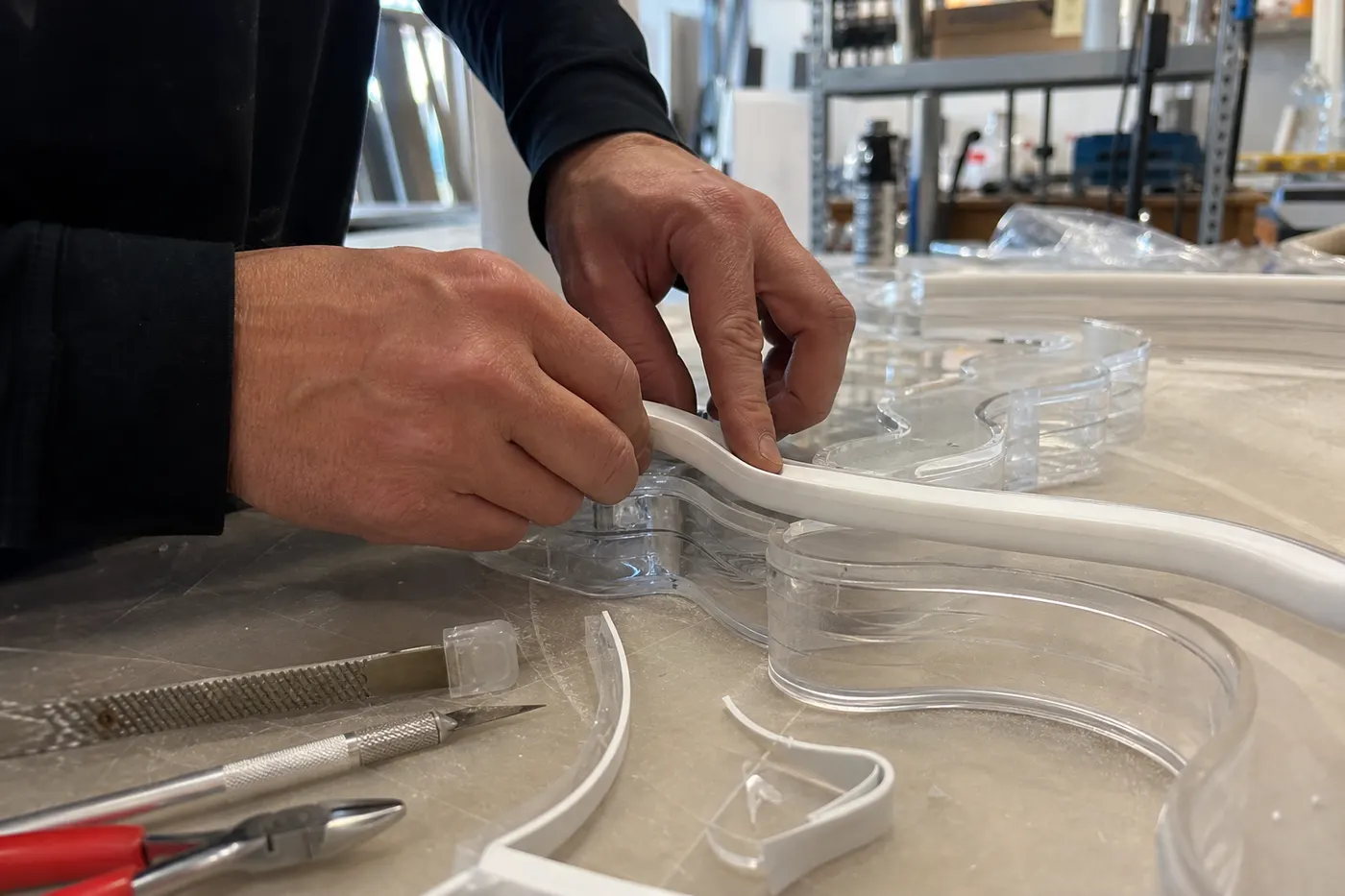 Hands fitting flexible LED neon tubing into a clear acrylic sign in a workshop