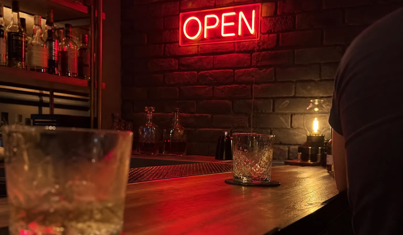 Red neon sign glowing on dark brick in a softly focused bar